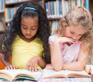 two young girls reading side by side in library